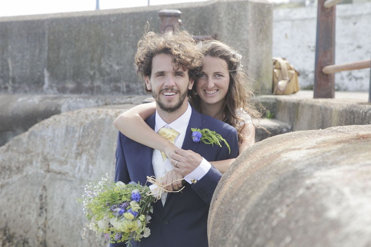 Candid moment of newlyweds laughing together by coastal stone wall.