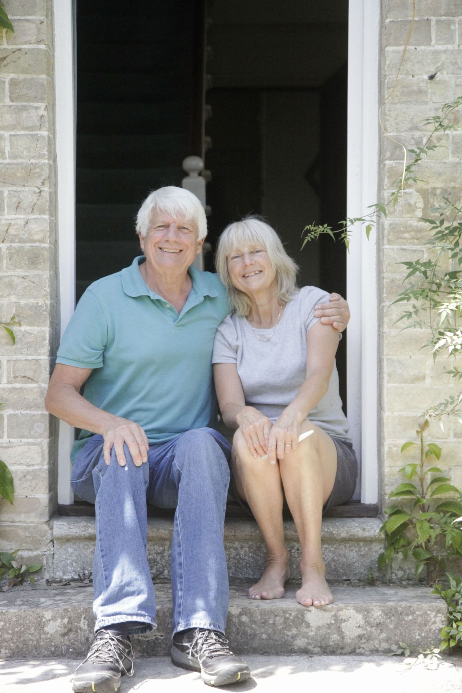 Senior couple sitting together on stone steps outside their home.