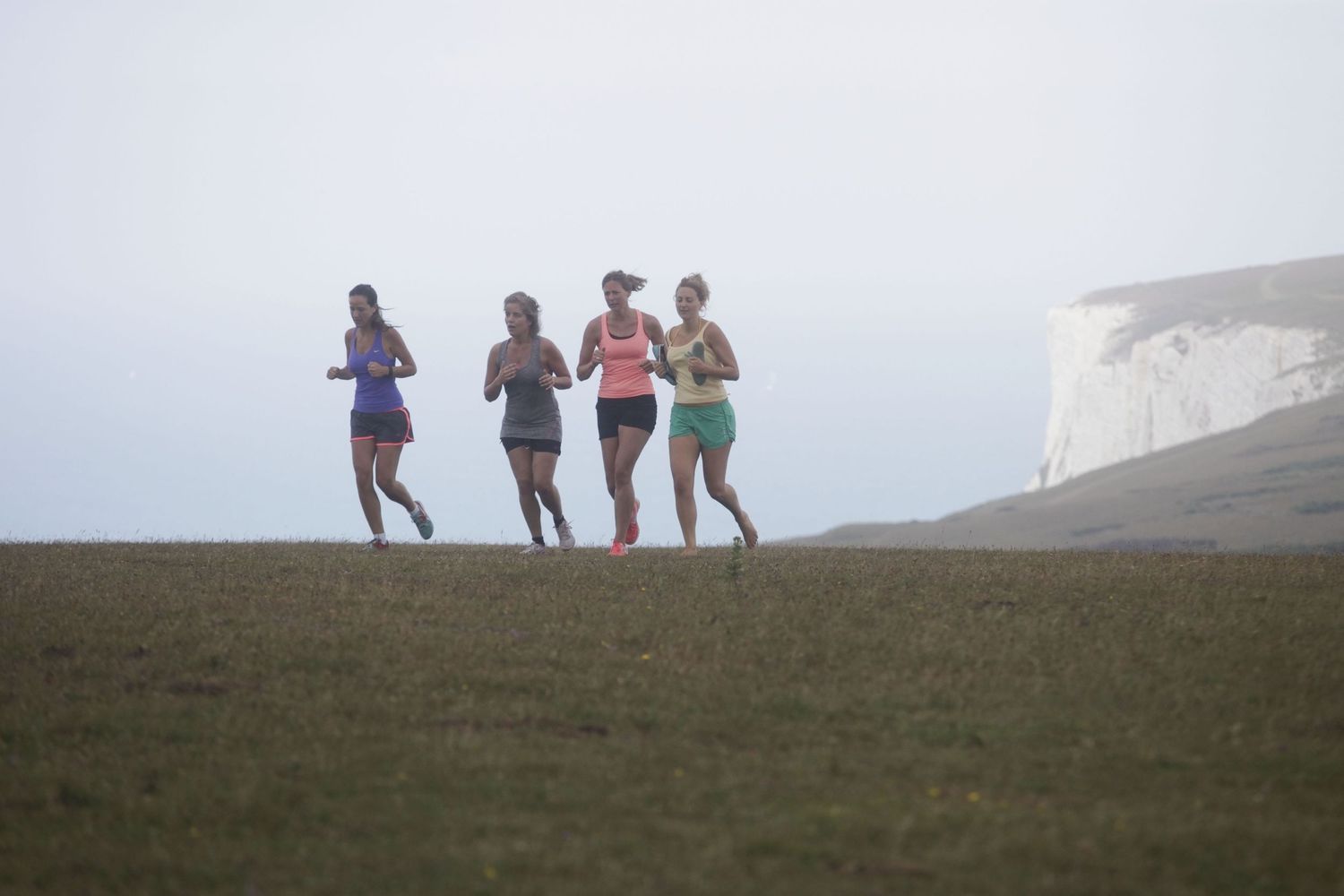 Silhouettes of hikers walking along ridge against misty coastal backdrop.