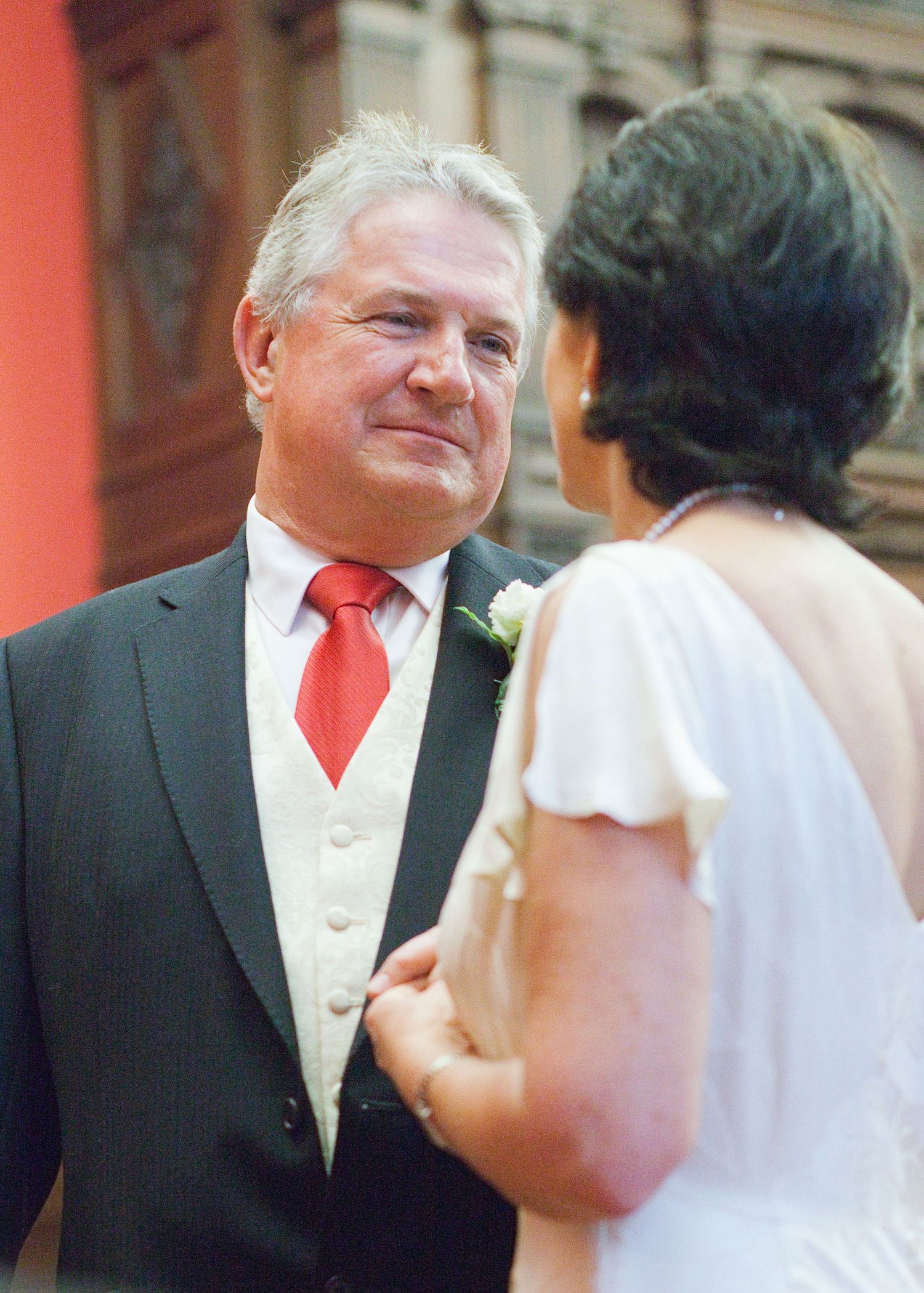 A formal couple walks together during a wedding ceremony with bright coral accents.