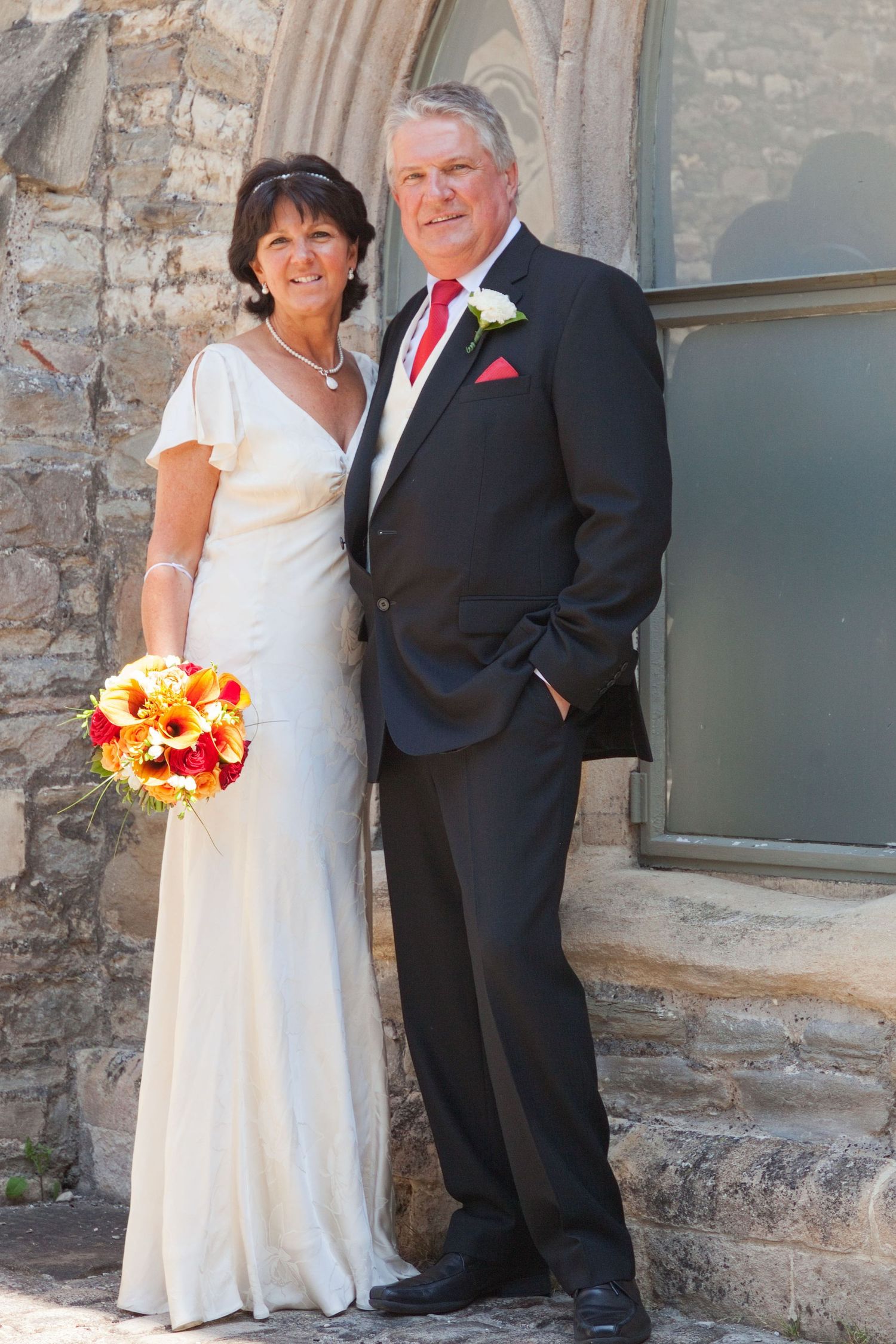 Wedding portraits taken against stone building with window and rustic architectural details.