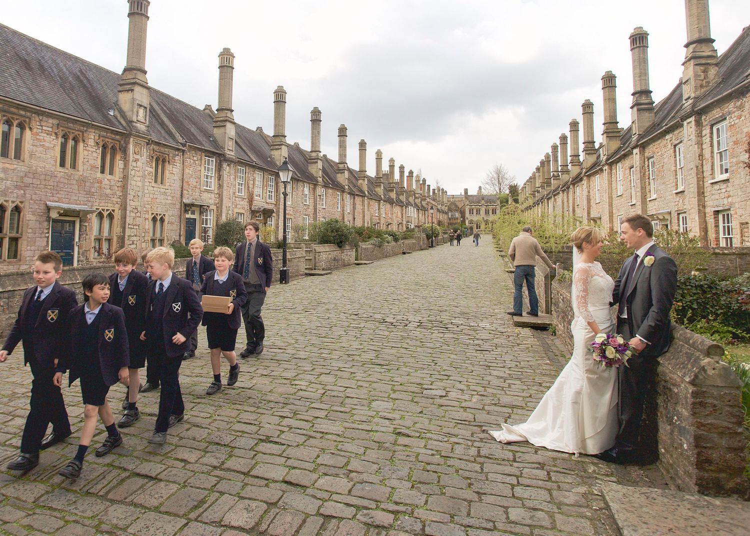 A cobblestone street lined with historic stone buildings and people gathered for a wedding celebration.