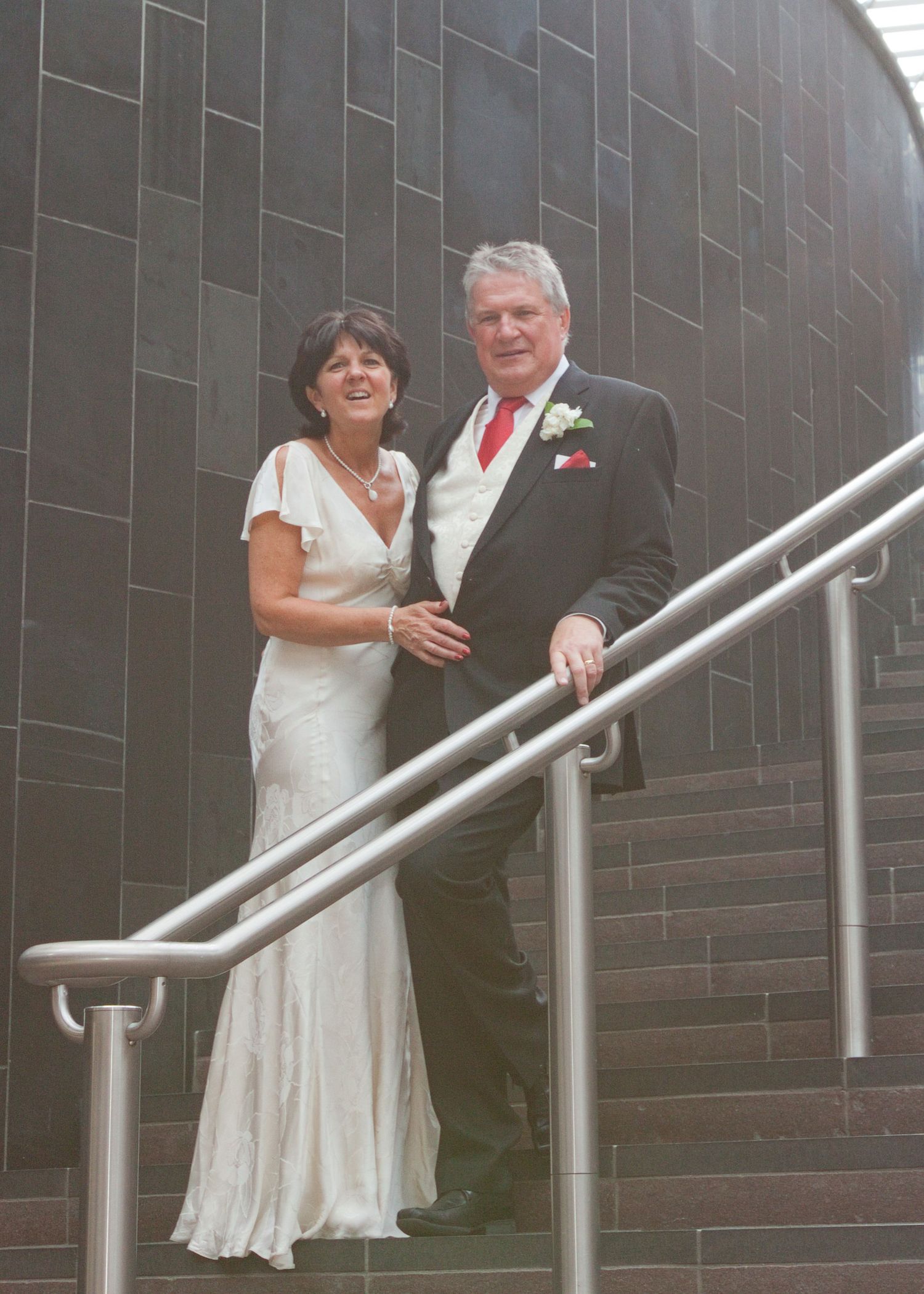 Couple descending modern metal staircase against dark tiled wall.