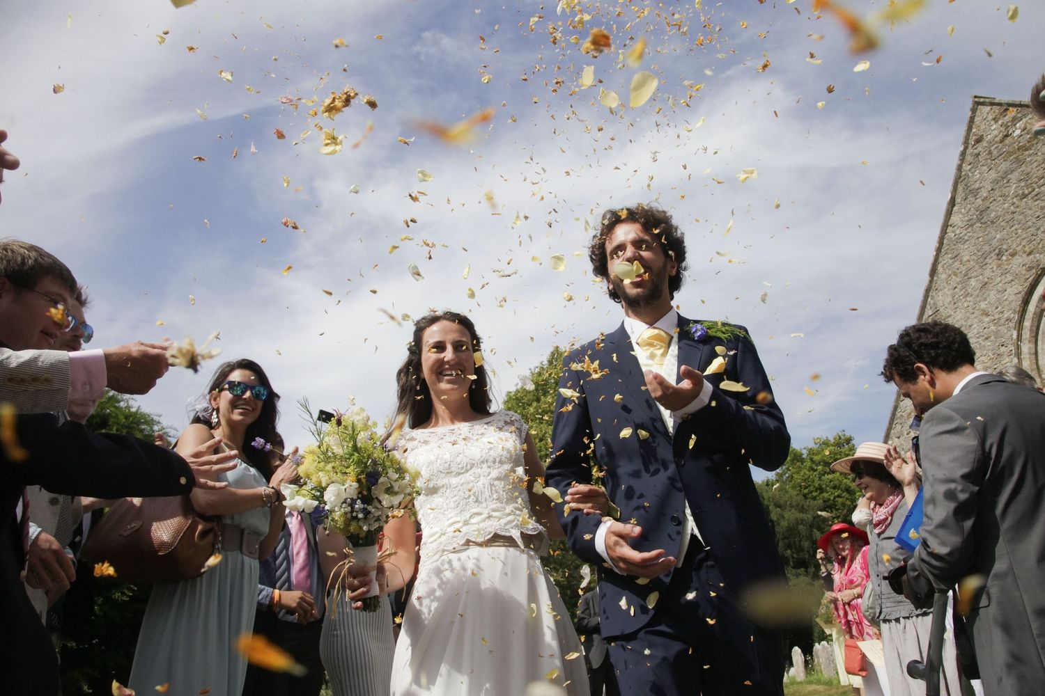 Colorful confetti fills the air as wedding guests celebrate outside a stone building.
