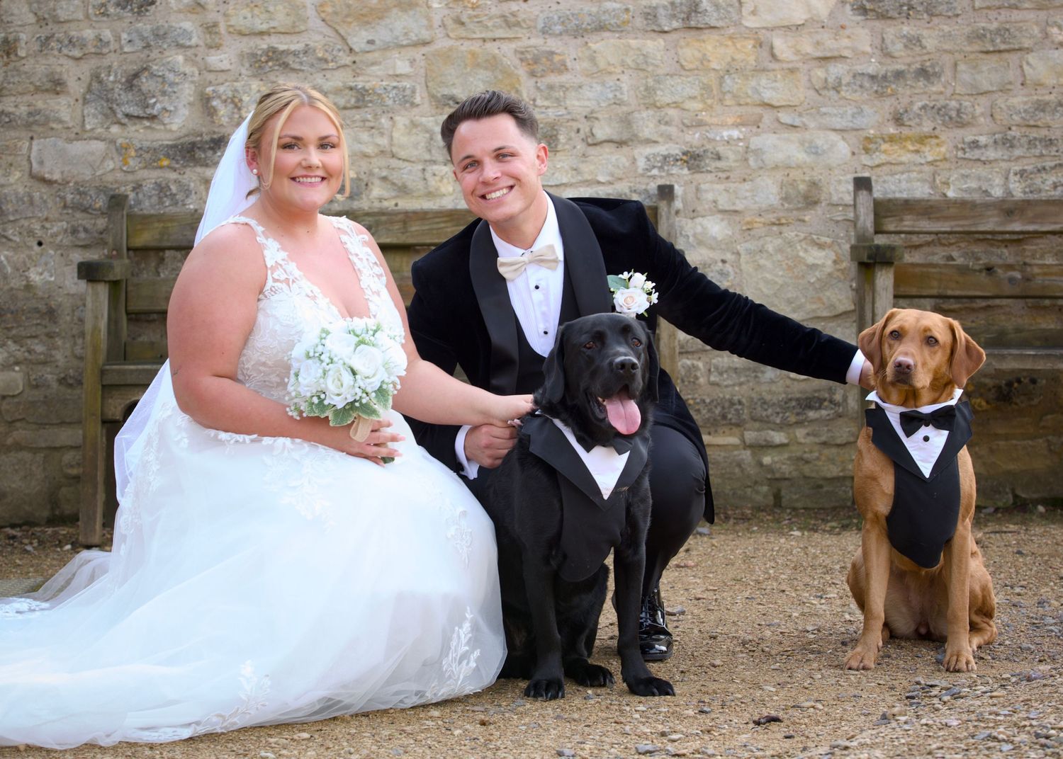 Wedding couple poses with their dog against rustic stone wall backdrop.