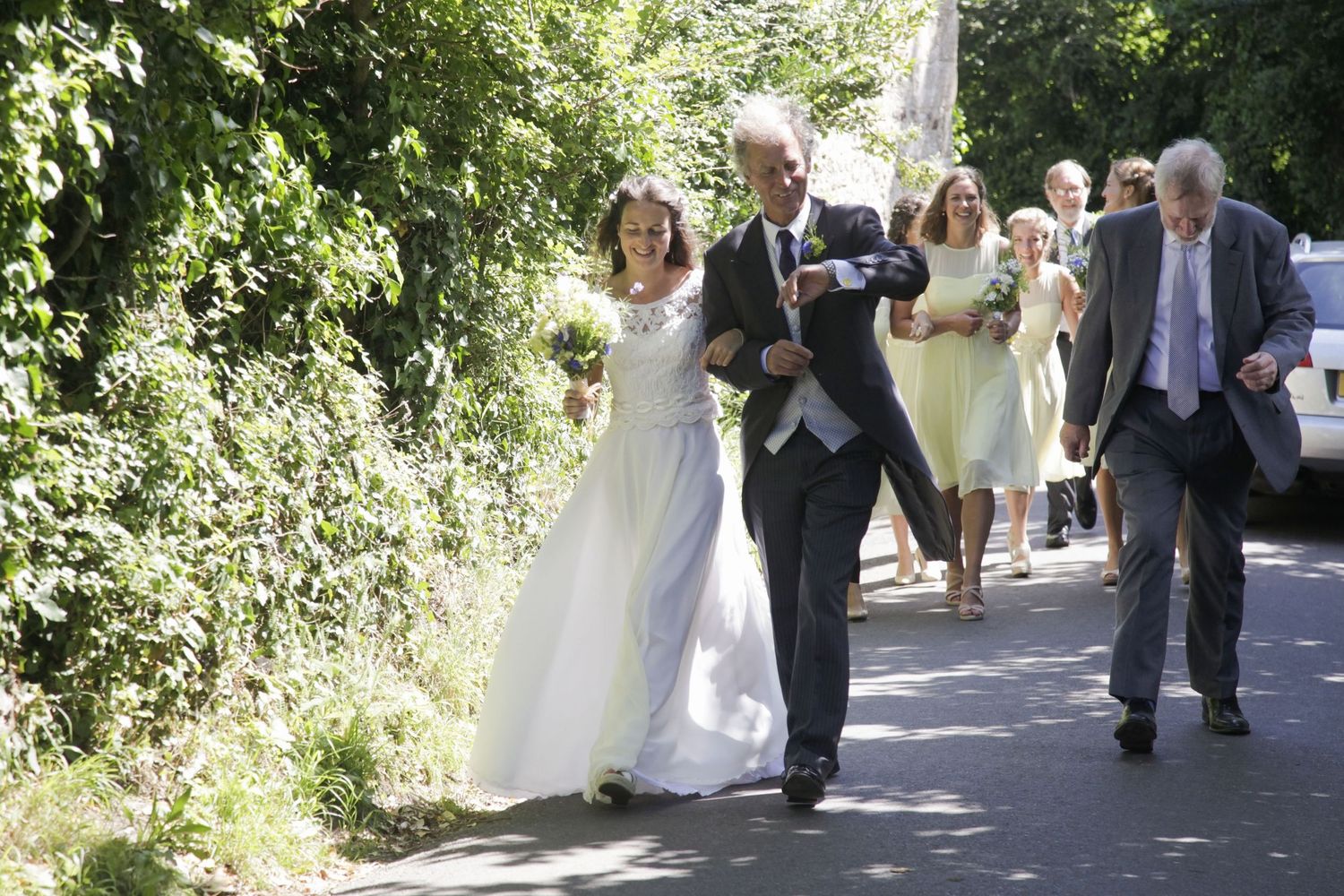 Wedding party proceeds down a garden path surrounded by lush greenery.