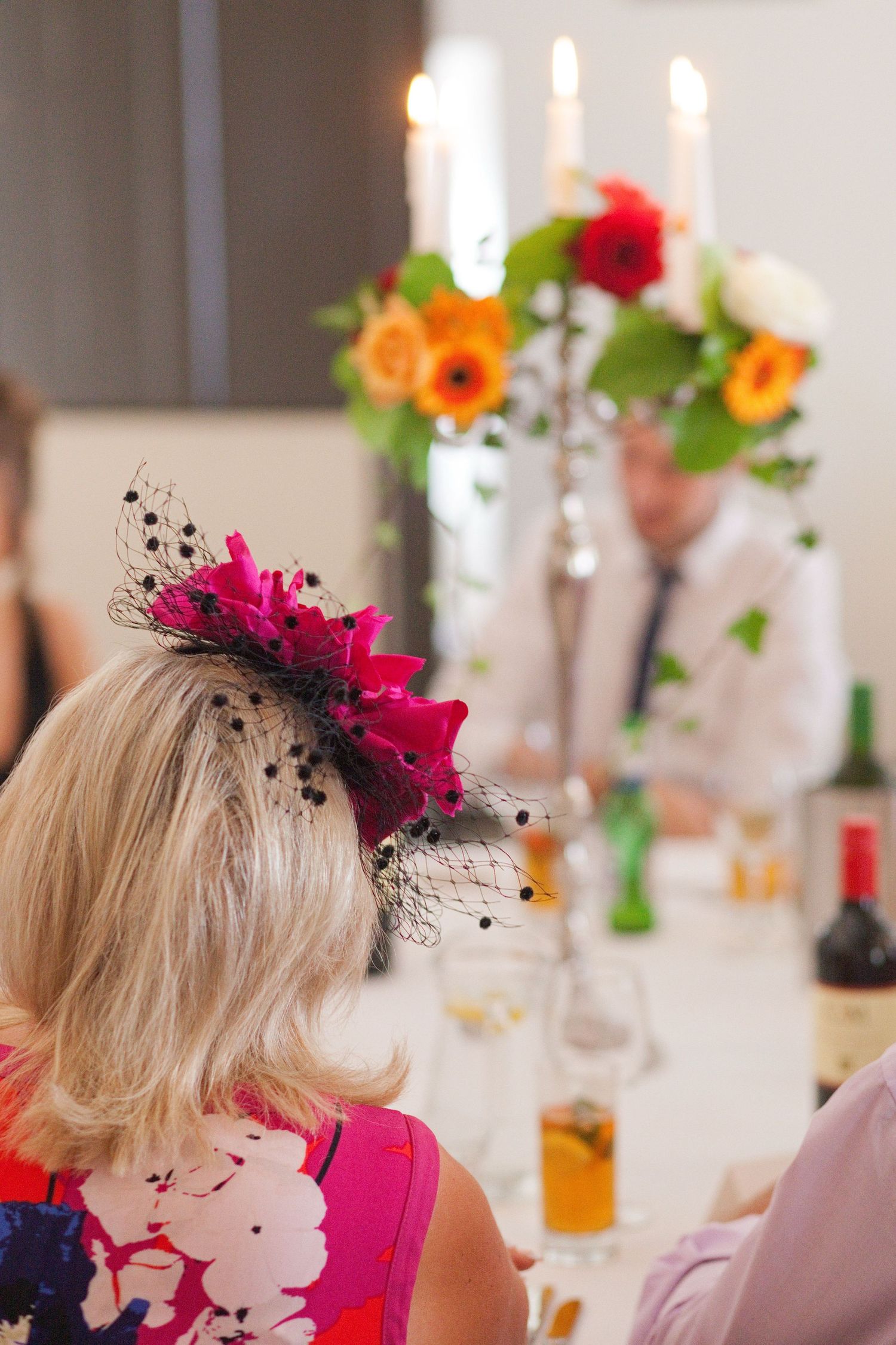 Wedding guests wearing bright pink fascinators enjoy a formal reception dinner in an elegant venue.