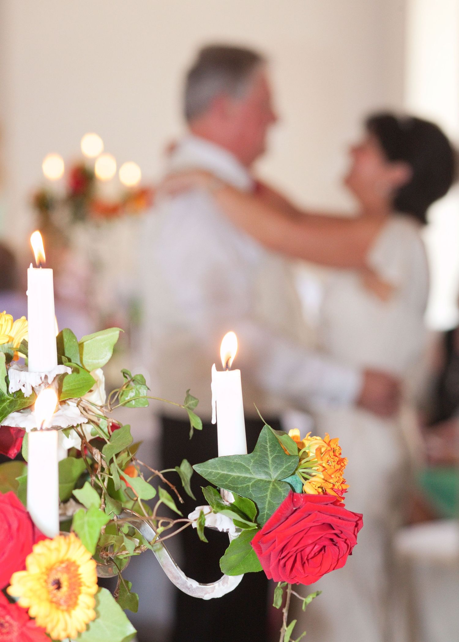 Table decorations with lit candles, red roses and yellow flowers at a wedding reception.