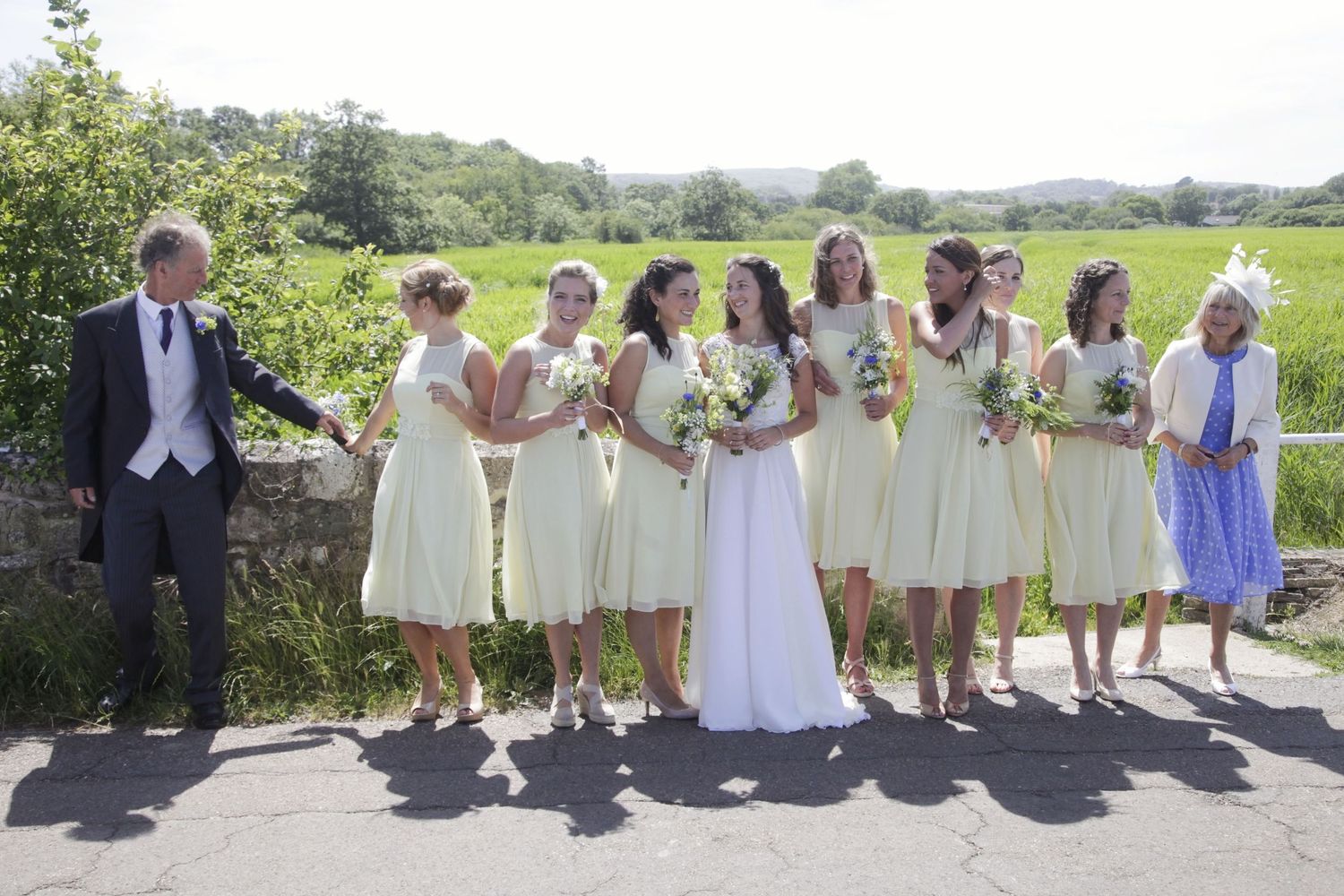 Wedding party members line up along a stone wall with rolling hills in the background.