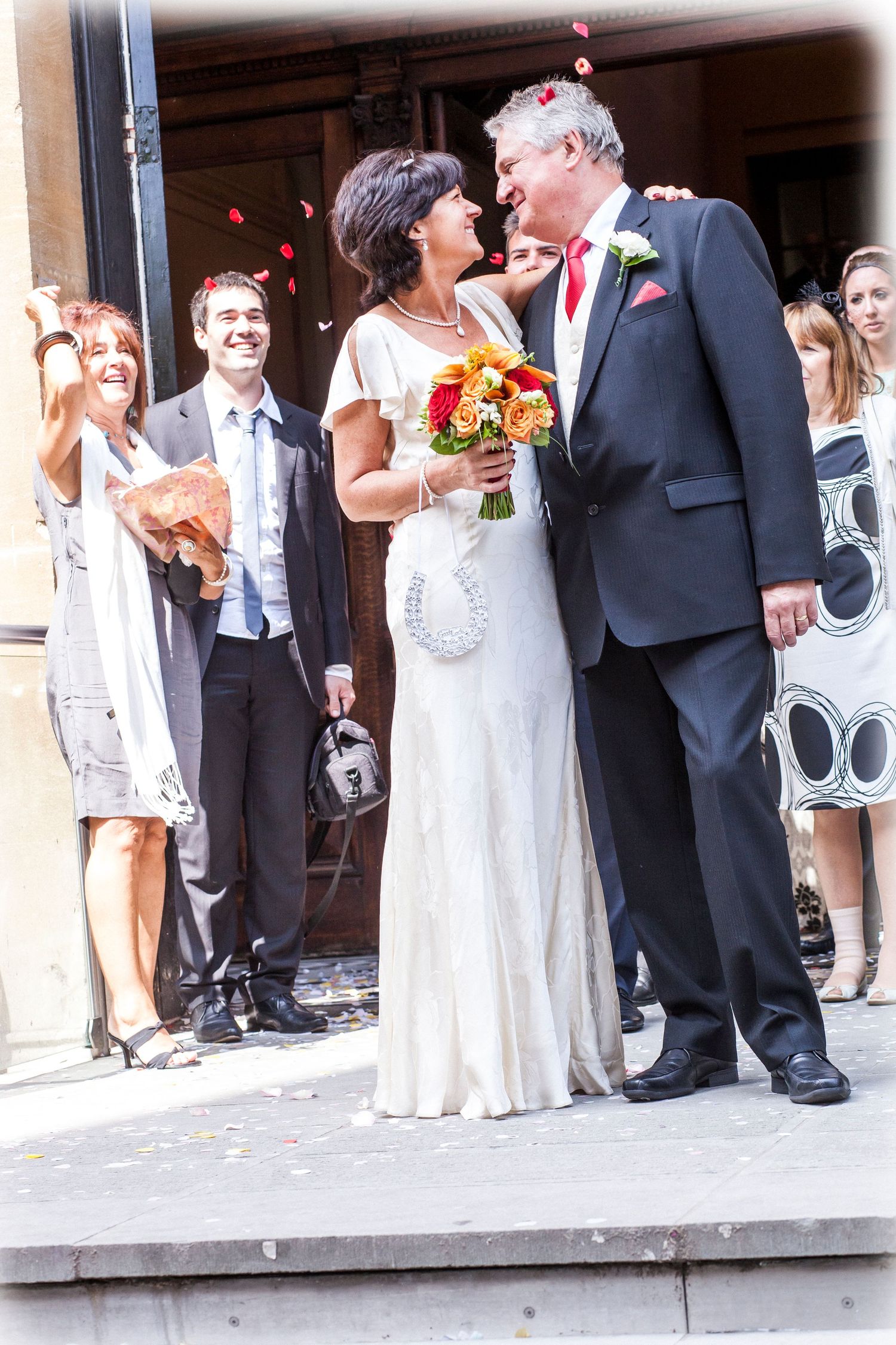 Newlyweds share an intimate moment on church steps as guests look on in Bath, England.