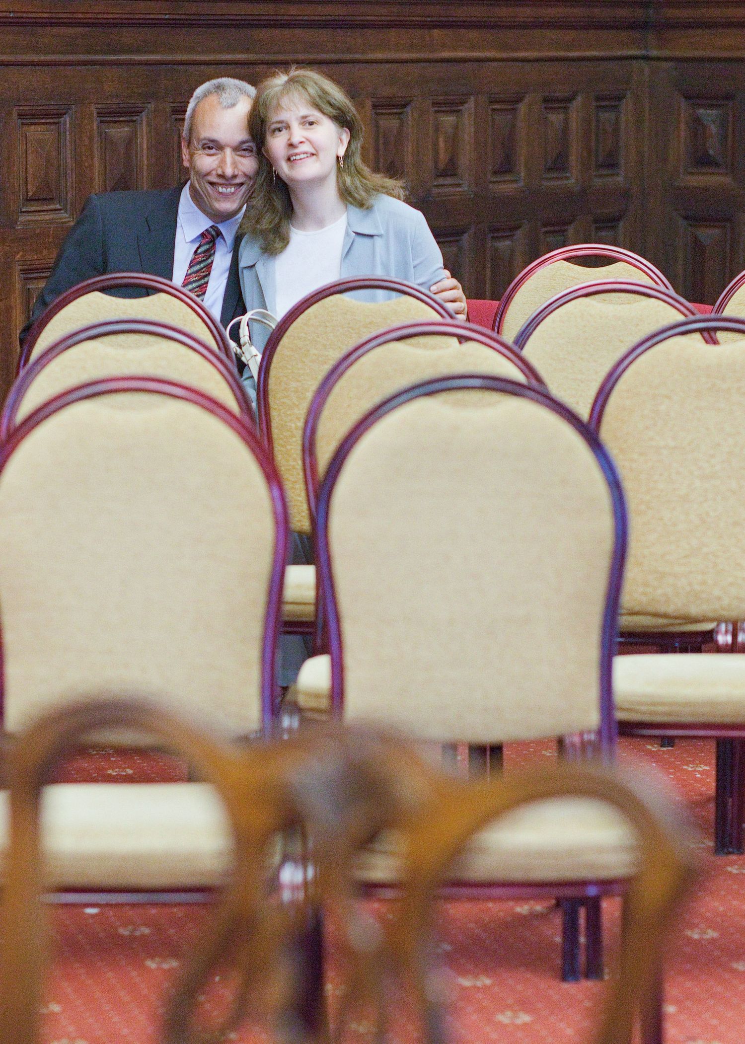 Wedding guests seated among rows of cushioned chairs in a formal indoor setting.