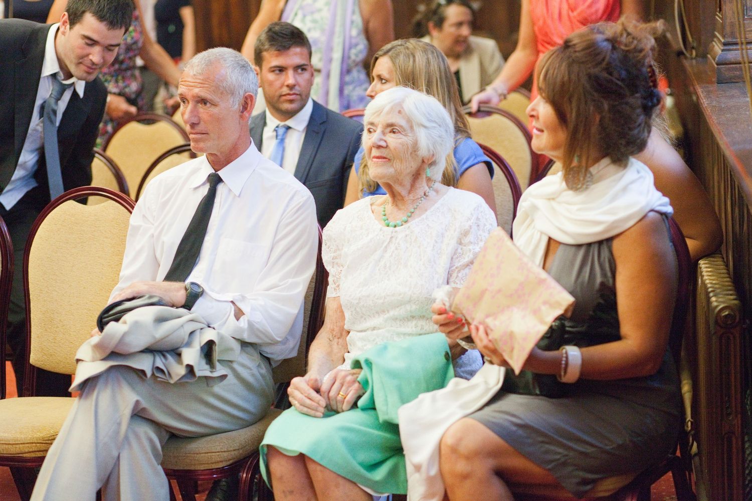 Wedding guests seated in cushioned chairs during an indoor ceremony.