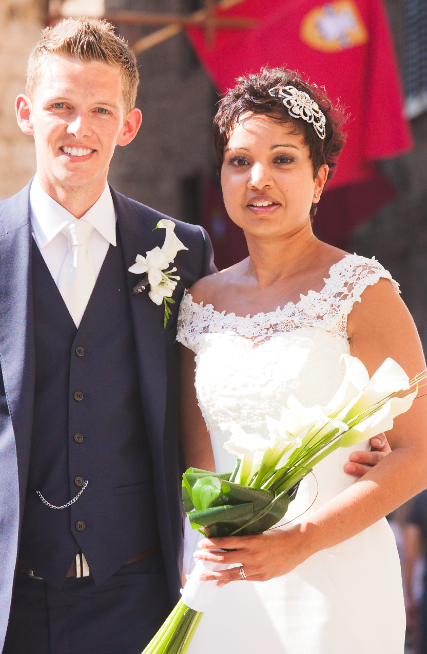 Newlyweds share a joyful moment in formal attire with white floral bouquet.