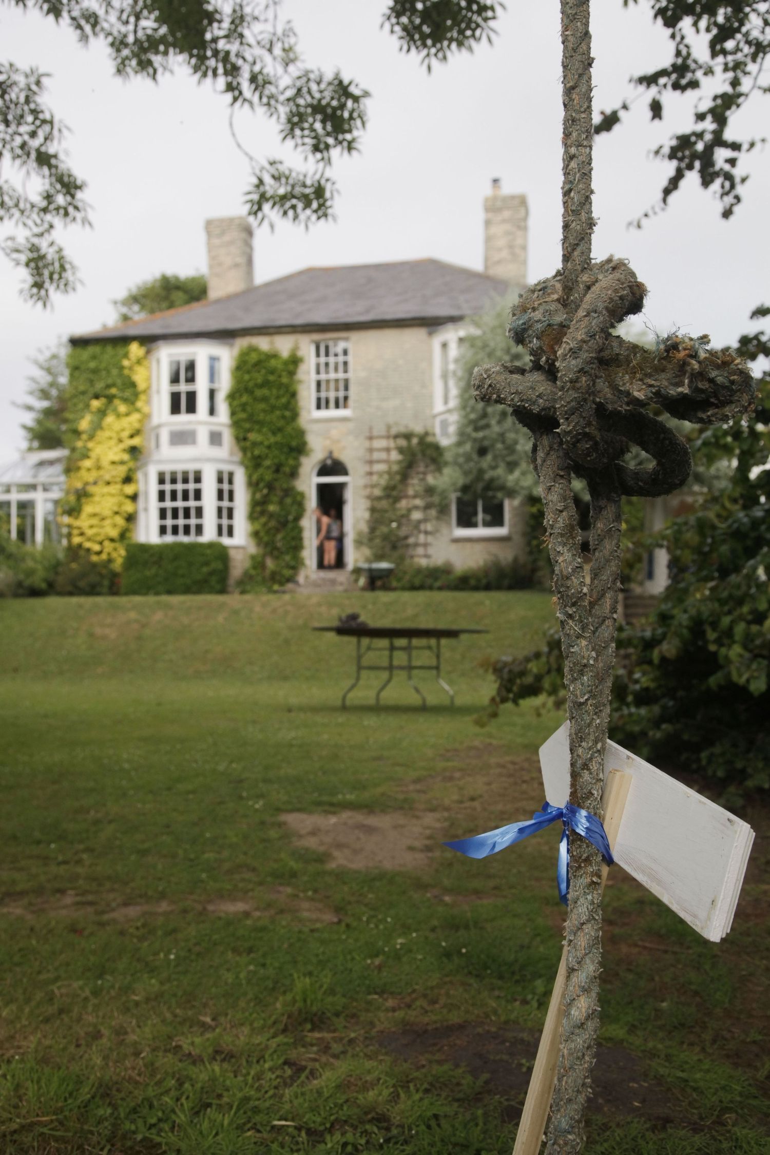 Stone house with large windows and manicured lawn surrounded by trees.