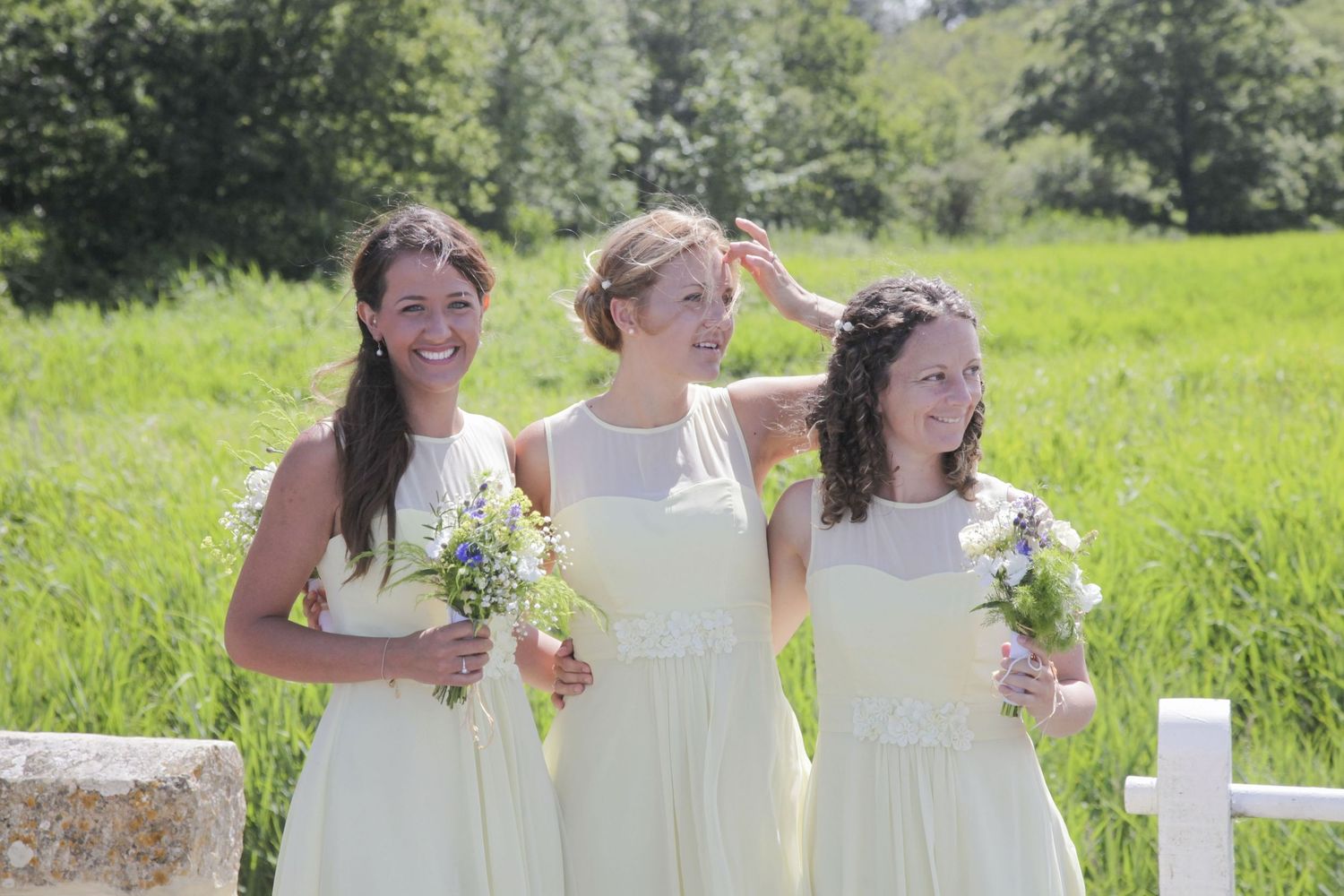 Bridal party members share joyful moments together in a sunlit meadow setting.