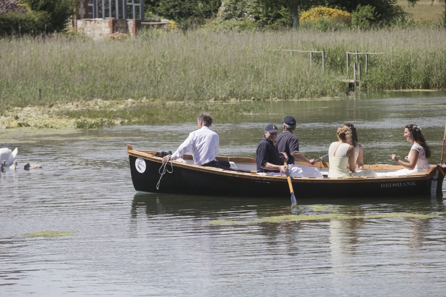 A traditional wooden canoe with passengers floats on a tranquil lake surrounded by marsh grass.
