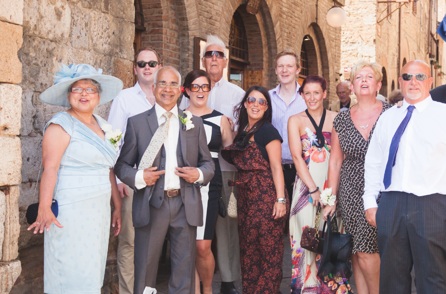 Wedding guests gather for a group photo against historic stone architecture.