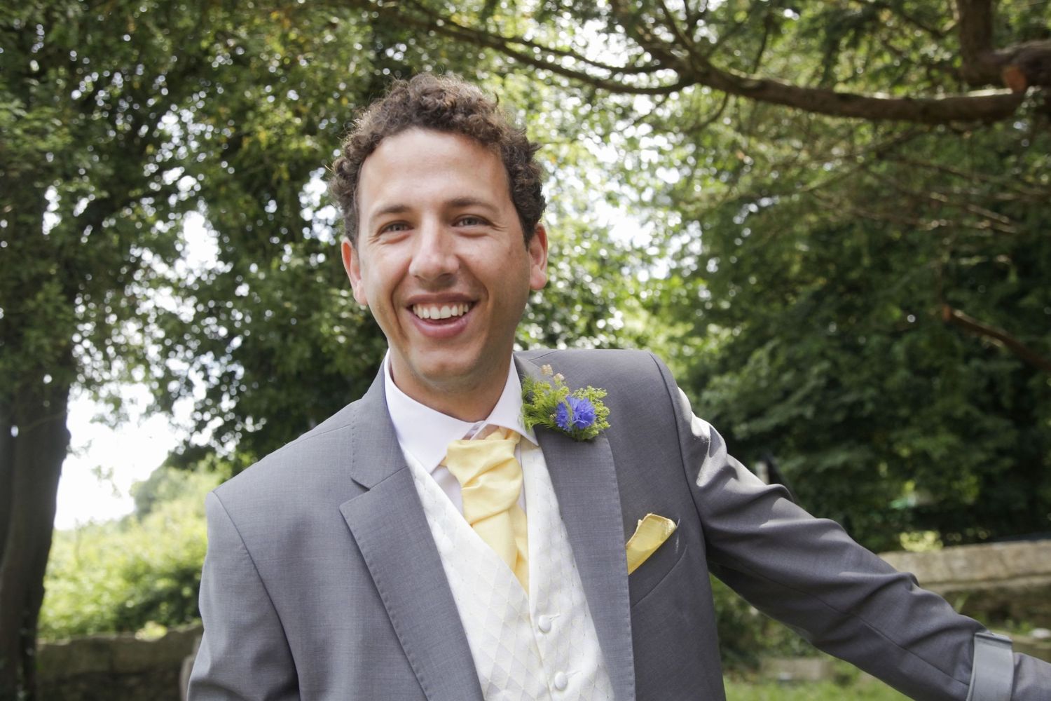 Groomsmen in gray suits with yellow ties smile outdoors.