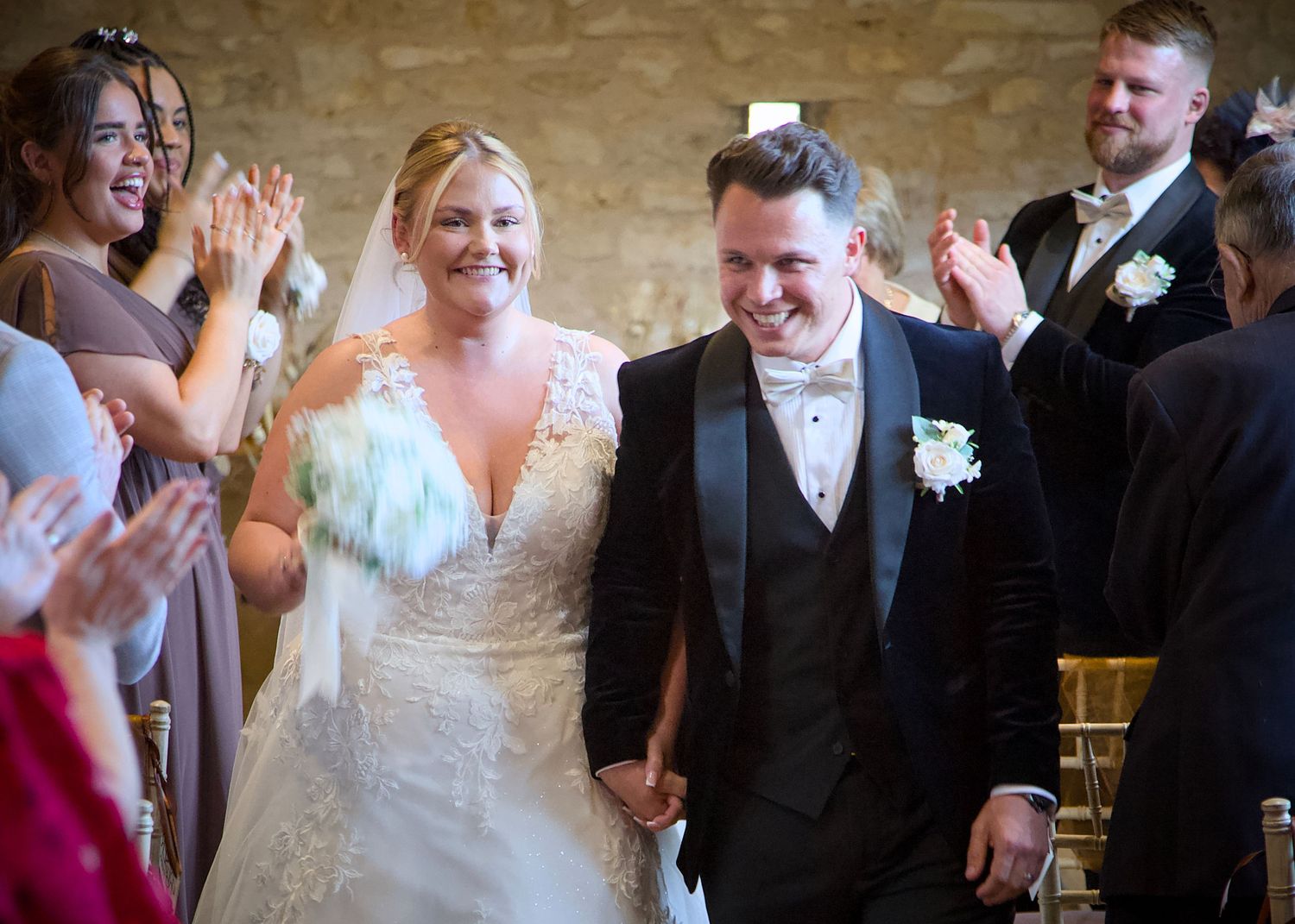 Wedding guests applaud as newlyweds walk down the aisle in celebration.