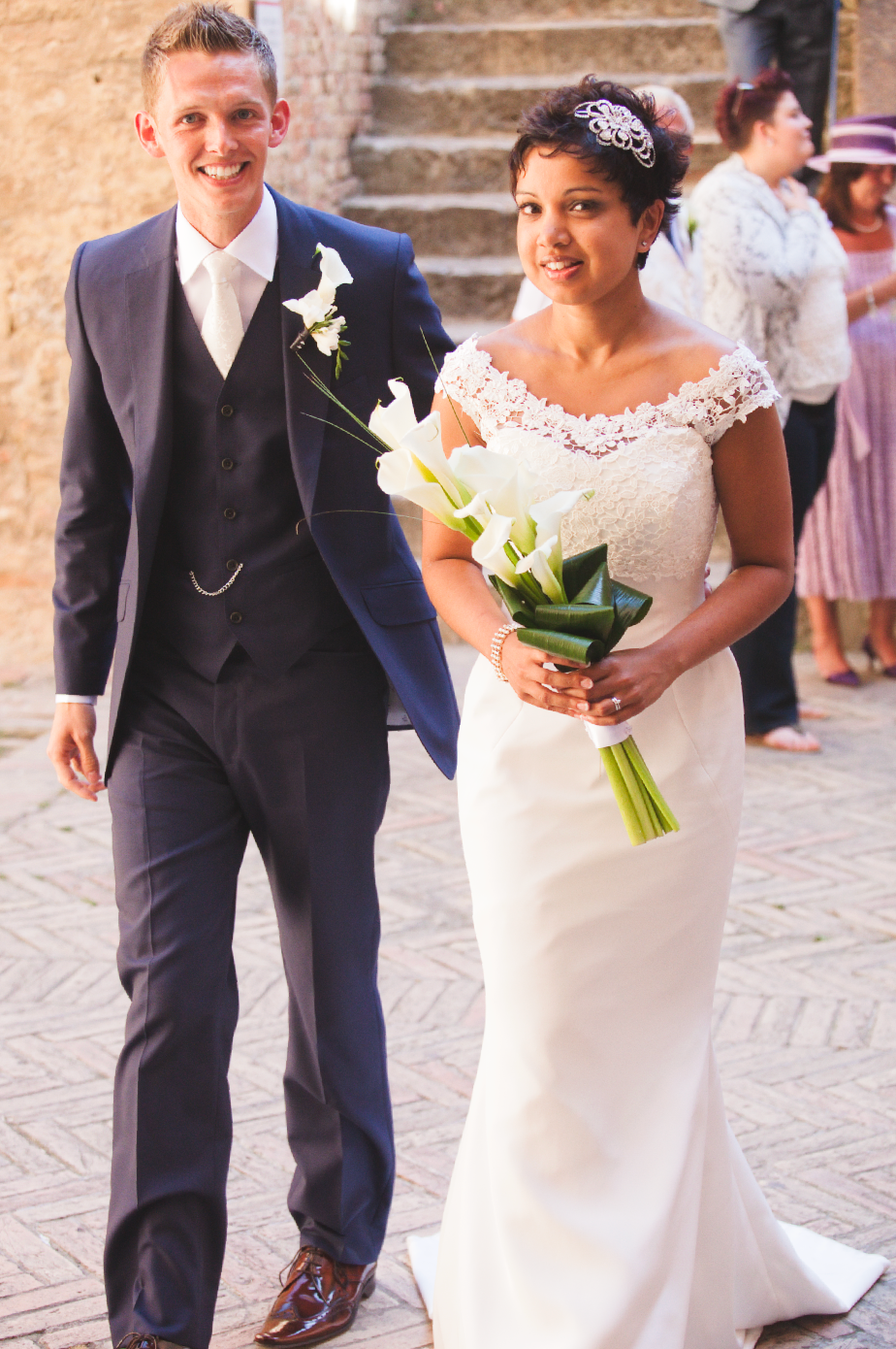 Newlyweds walk together through a rustic stone archway during their wedding ceremony.