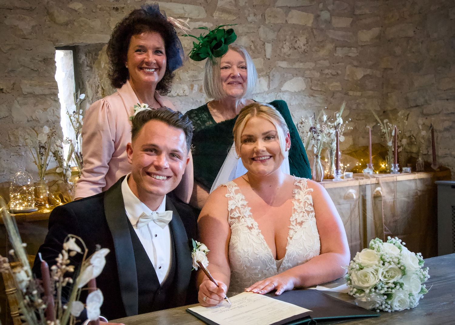 Wedding couple signing marriage documents while guests celebrate in a stone-walled venue.