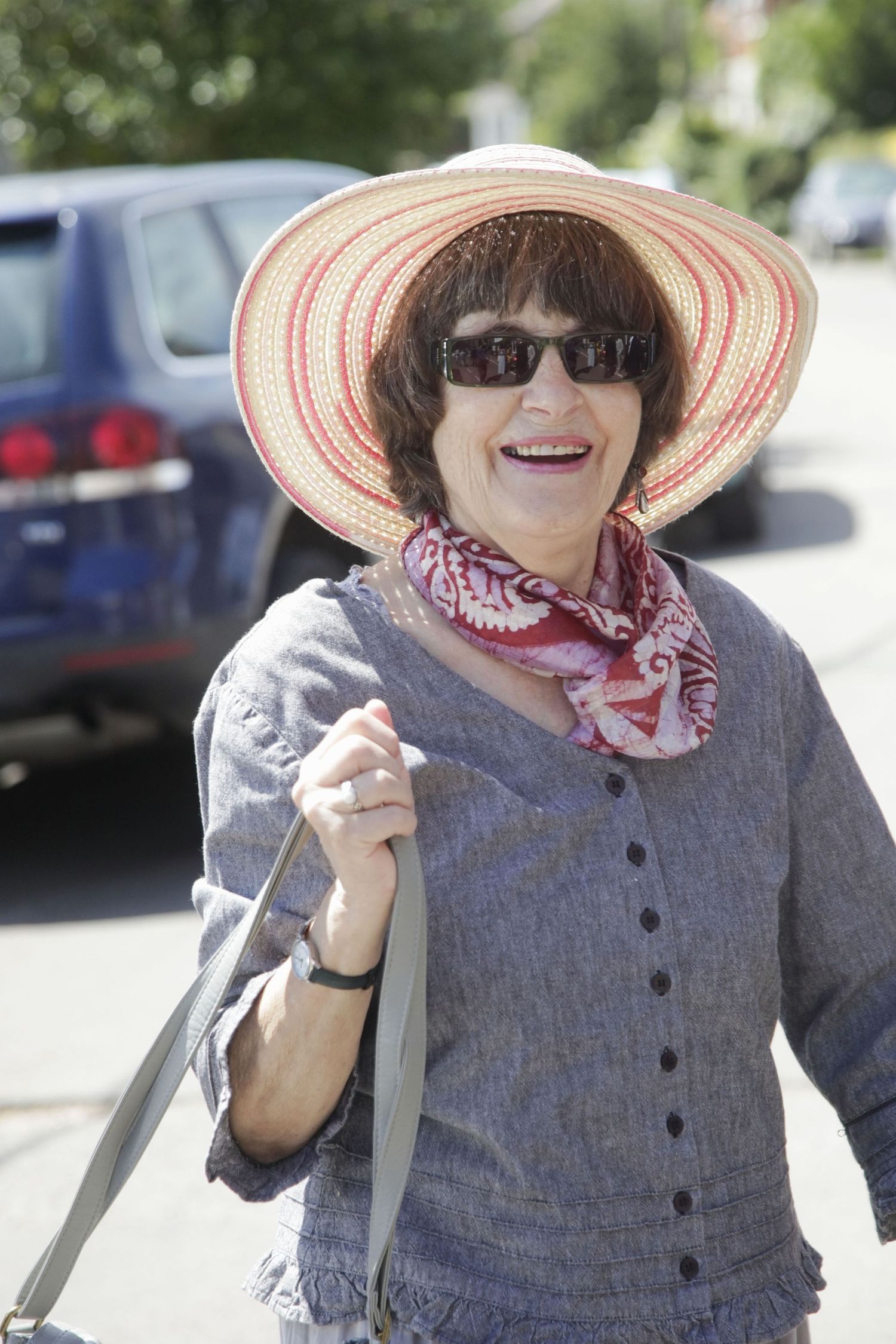 Person wearing a striped sun hat and gray button-up outfit smiles outdoors.