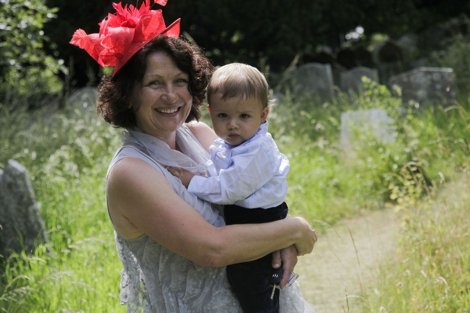 Wedding guests gather in a sunny churchyard with red flowers.