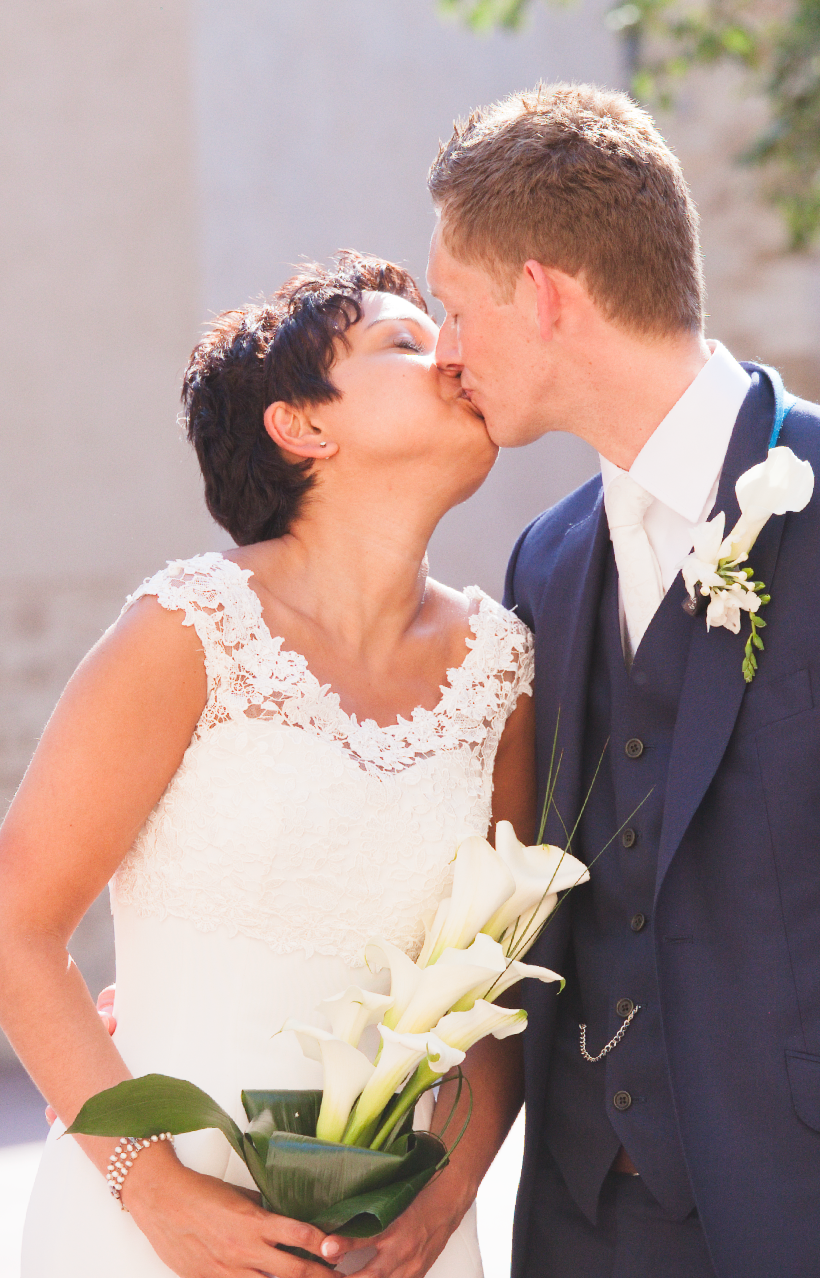 Close up of wedding couple with white lily bouquet in bright sunlight.