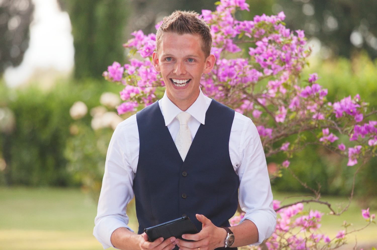 Wedding party members in formal attire laughing during outdoor celebration.