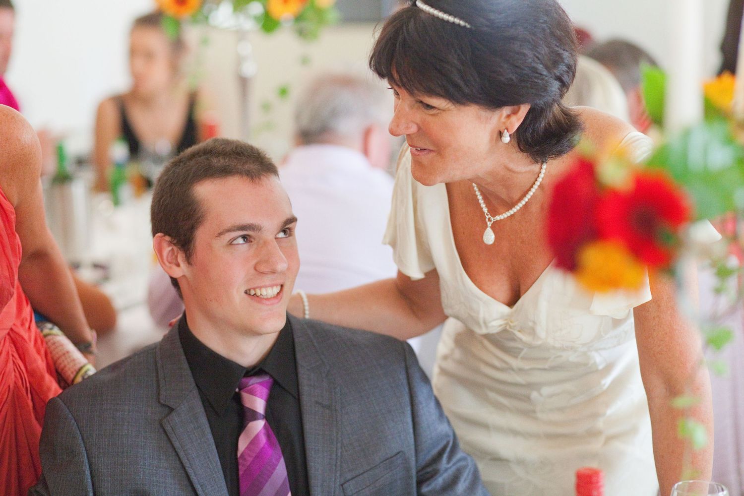 Wedding reception guests enjoying conversation at tables decorated with vibrant orange and red flowers.
