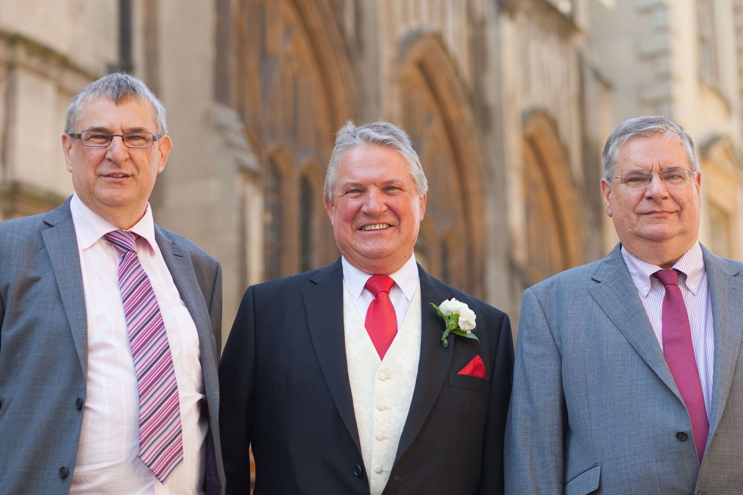 Three men in formal attire stand together at a wedding celebration.