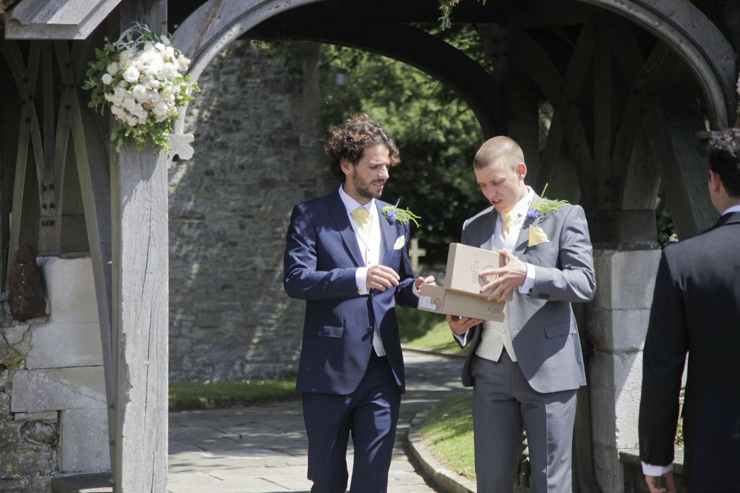 Wedding guests in formal attire socializing under a stone archway.