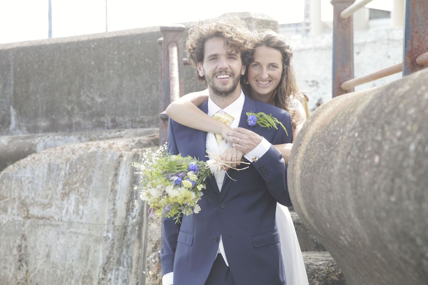 Wedding couple shares playful moment along seaside stone pathway.