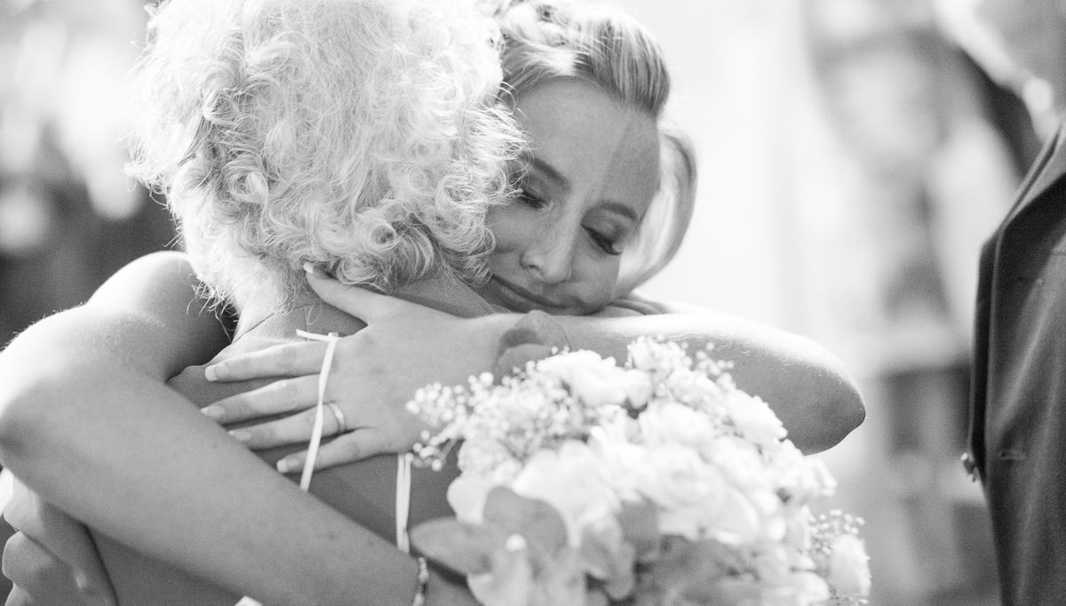 Black and white wedding photo capturing an emotional embrace with bouquet.