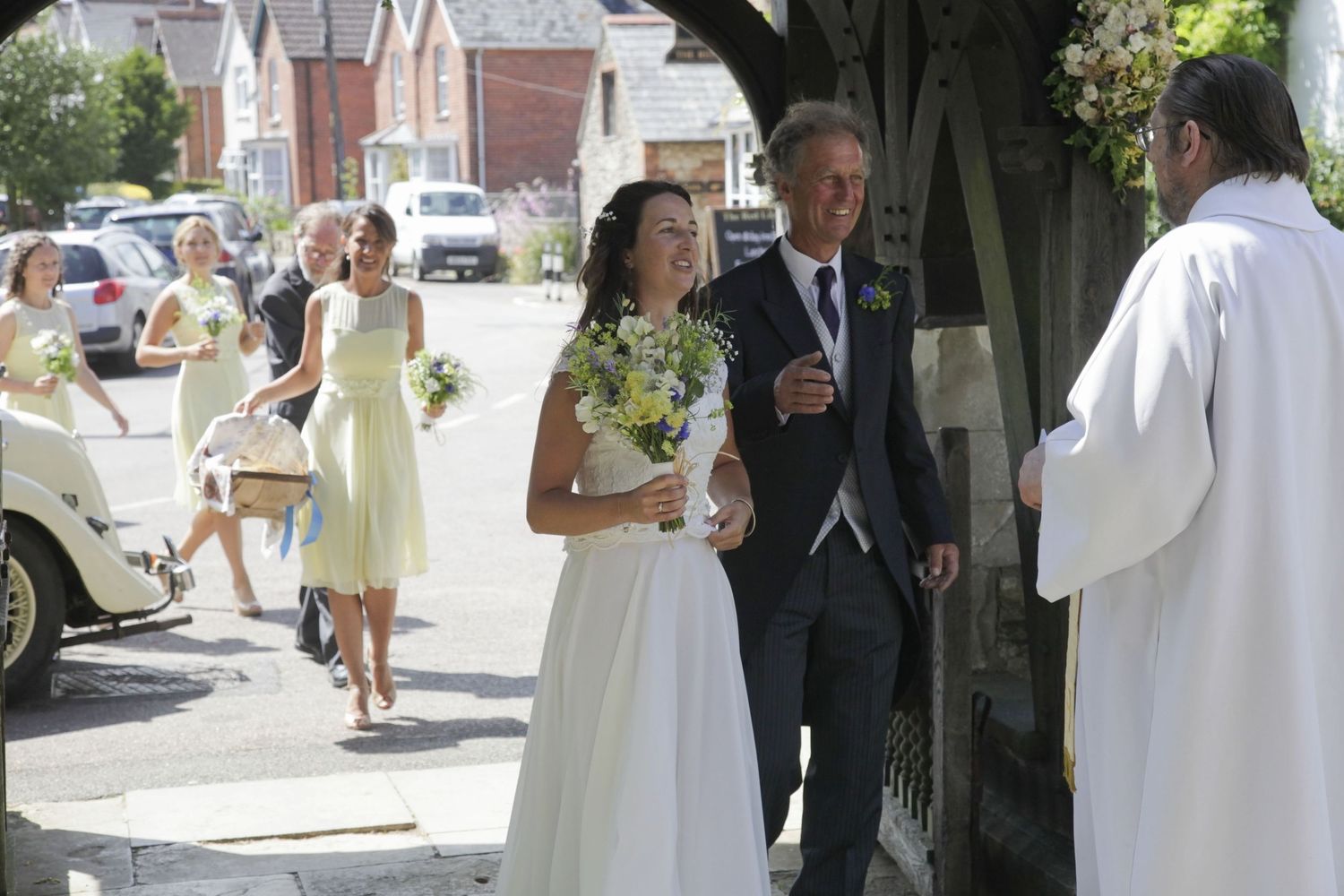 Wedding ceremony taking place under a church archway with yellow-dressed attendants.