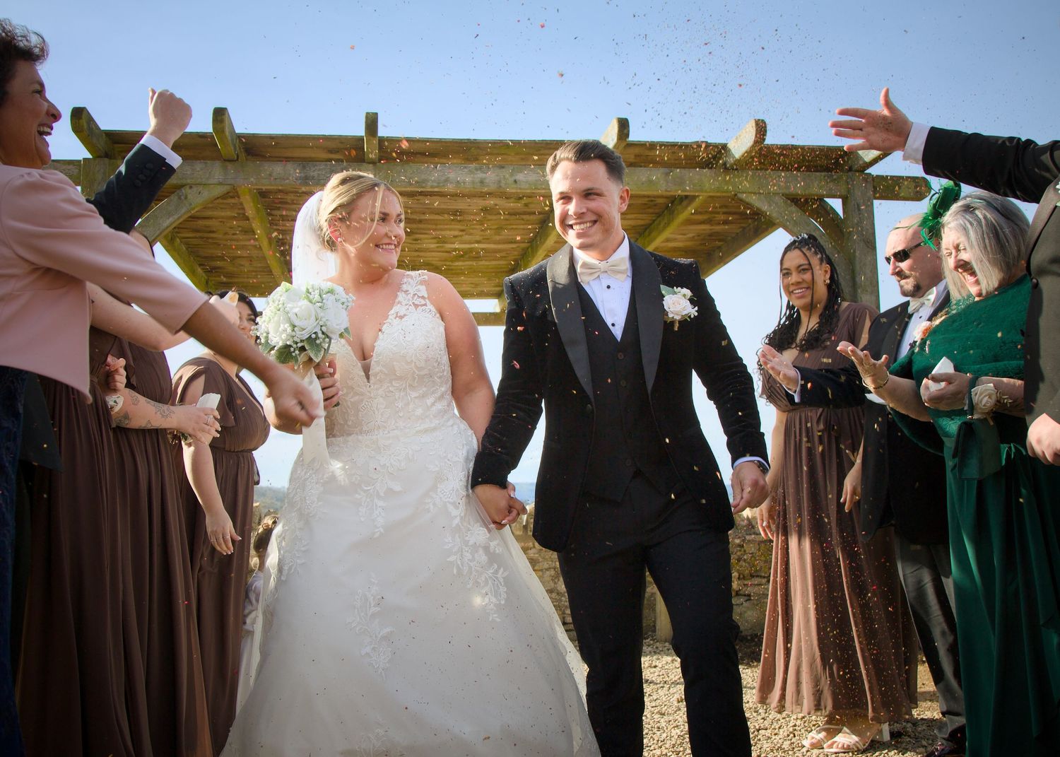 Wedding celebration with guests throwing confetti outdoors.