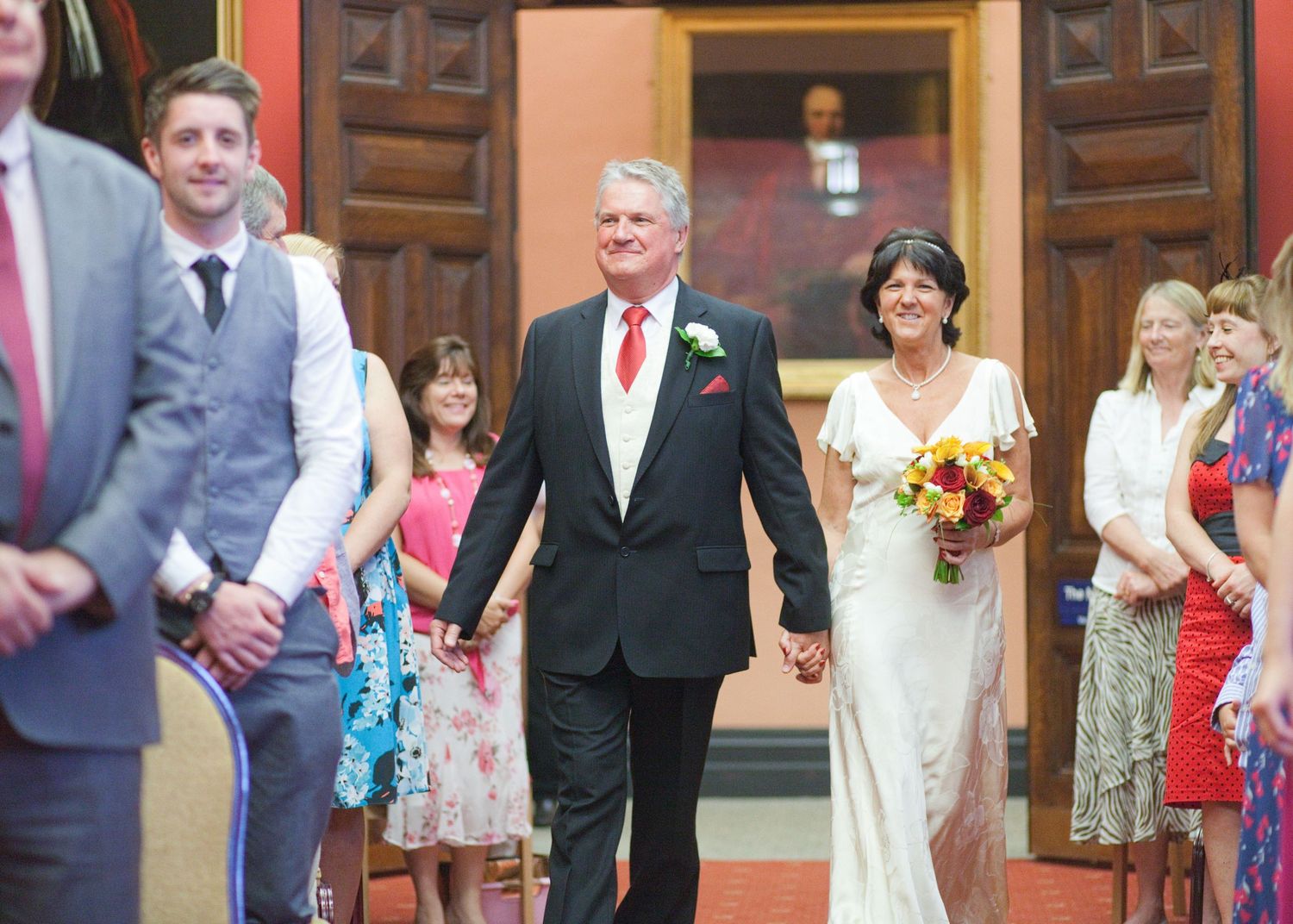 Wedding guests walk through an elegant venue with coral walls and wooden trim.