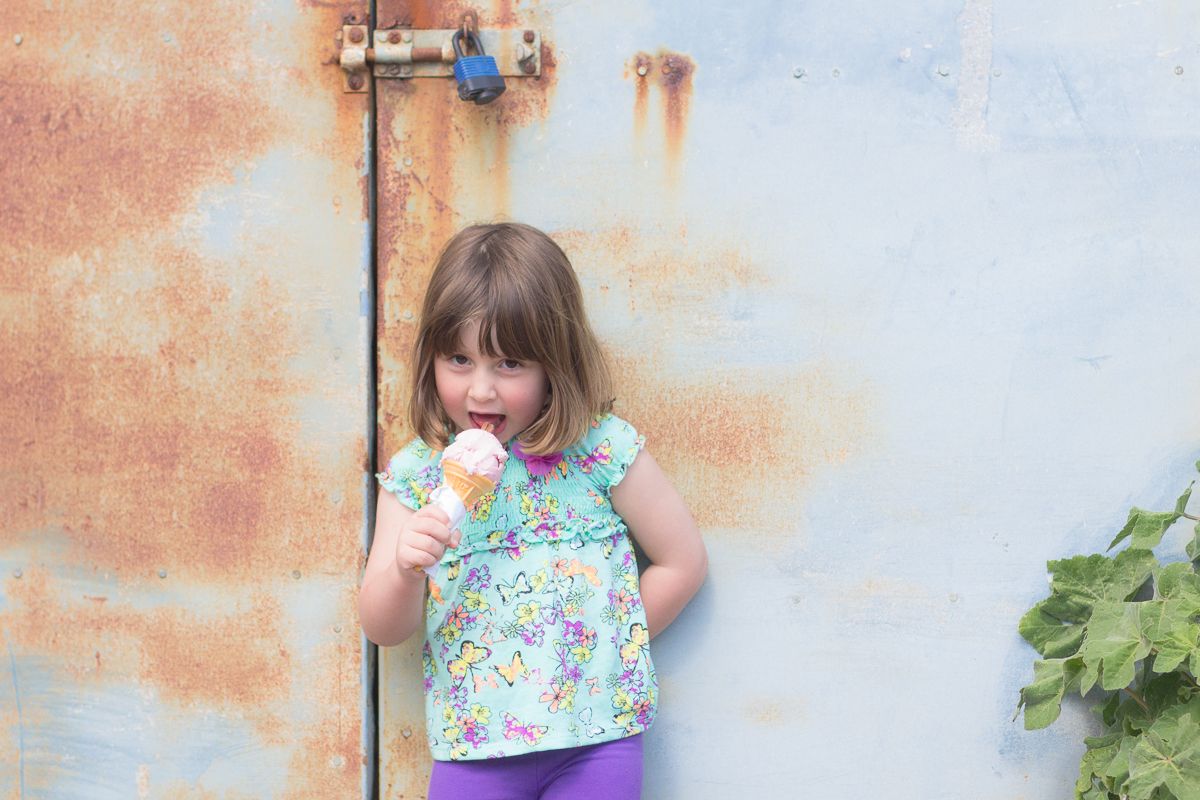 A person in a colorful floral top poses against a peach-colored wall next to green foliage.