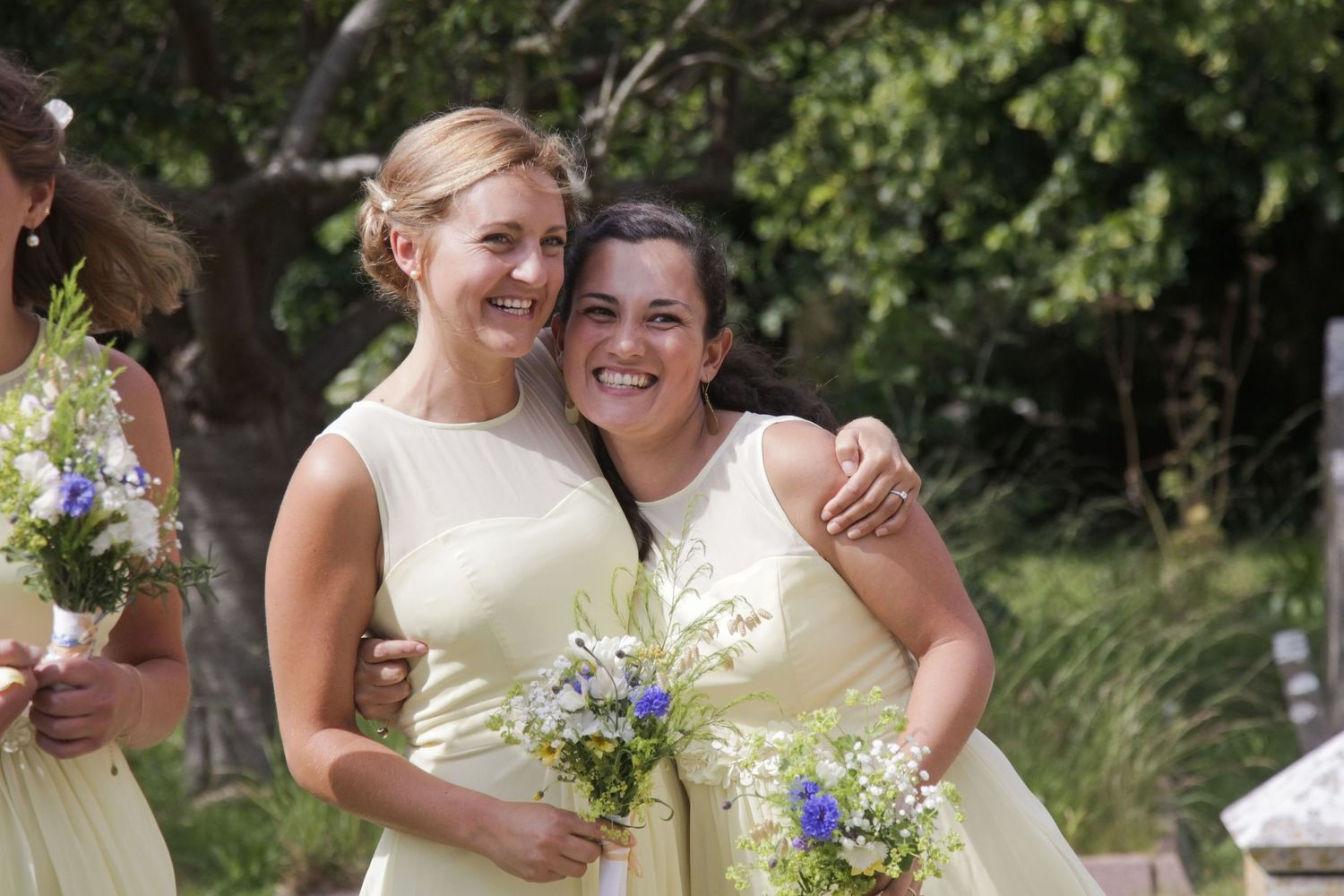 Wedding party members smile and celebrate outdoors near a stone wall.