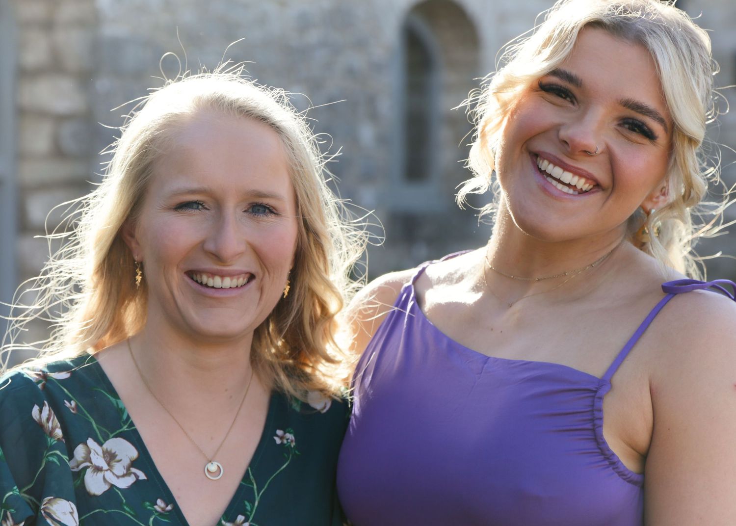 Group of women in purple and green dresses pose together outdoors.