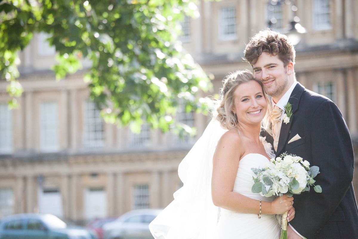 Sunny outdoor wedding portrait with historic building backdrop.