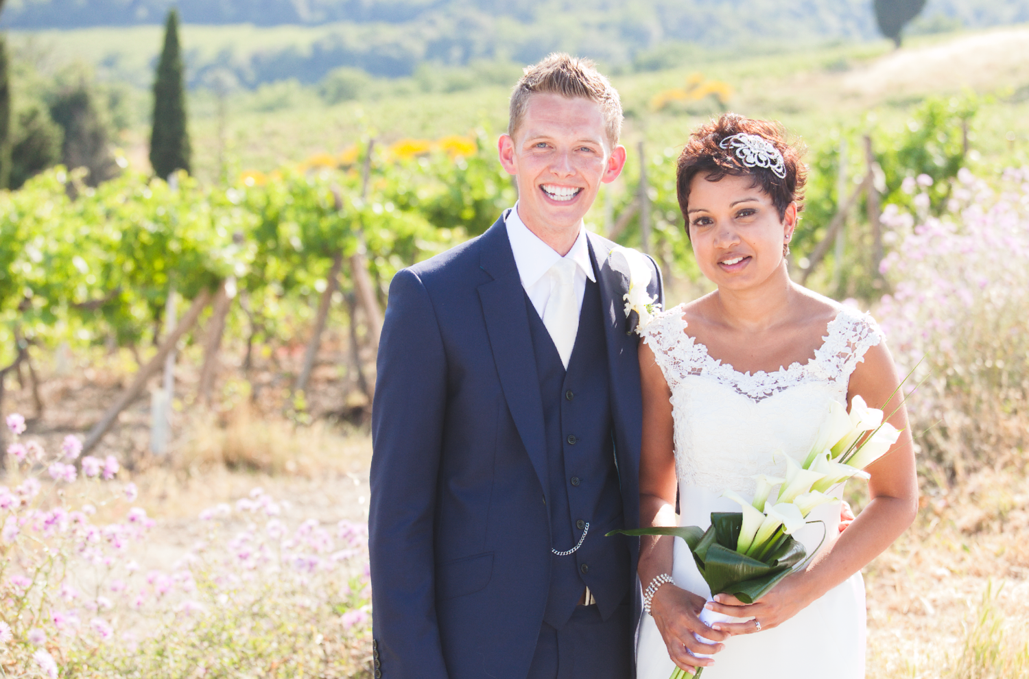 A sunny wedding portrait taken in a beautiful vineyard with rolling hills in the distance.