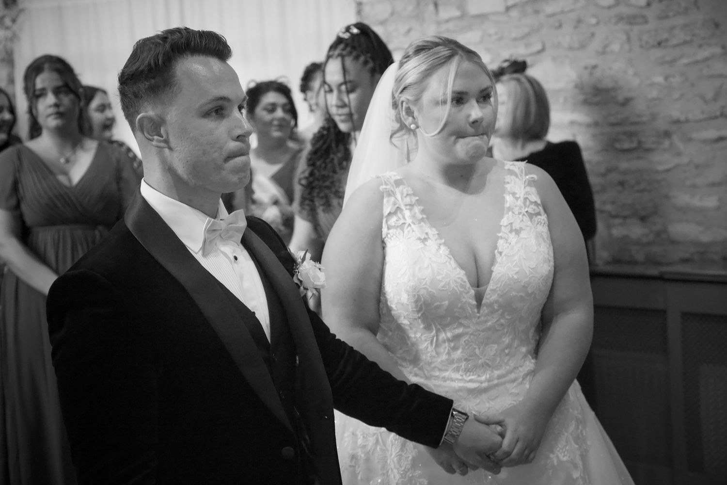 Candid black and white shots of wedding ceremony interactions in a brick-walled venue.