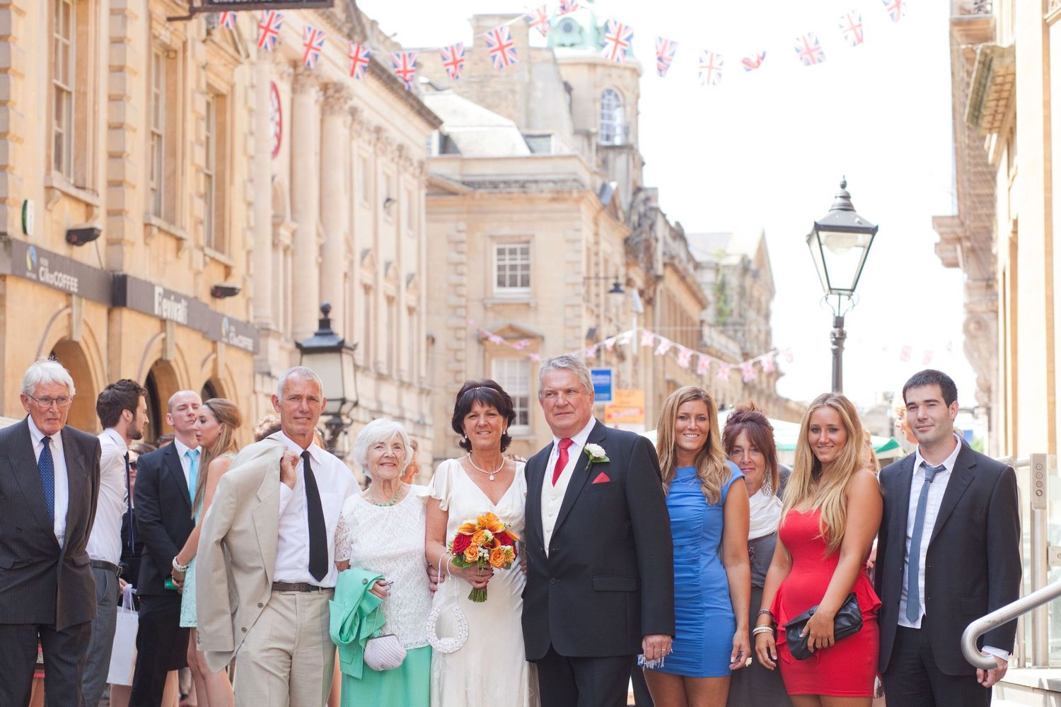Wedding party and guests line up along a charming street with bunting decorations overhead.