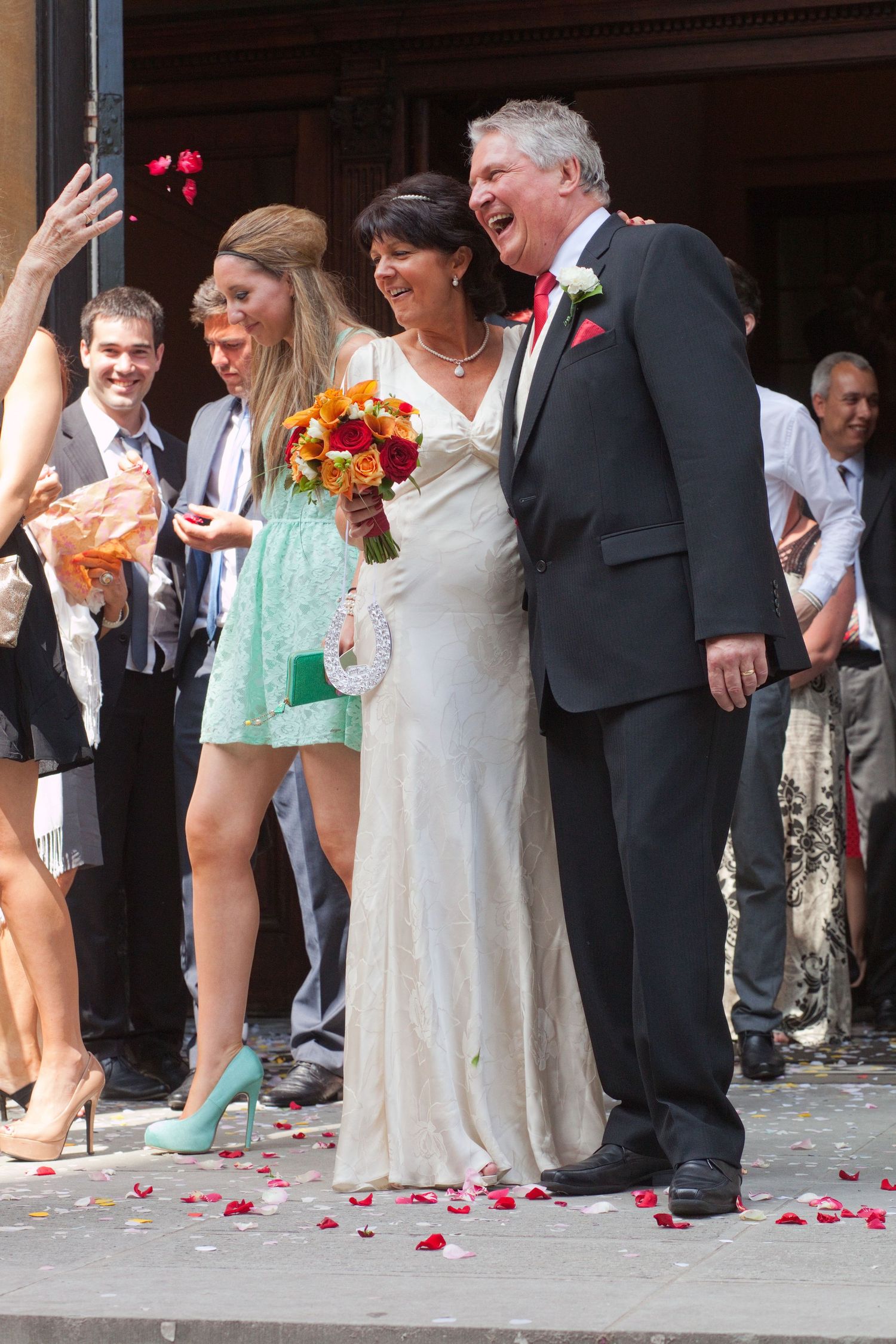 Wedding guests celebrating with the newlyweds on steps as rose petals fall.