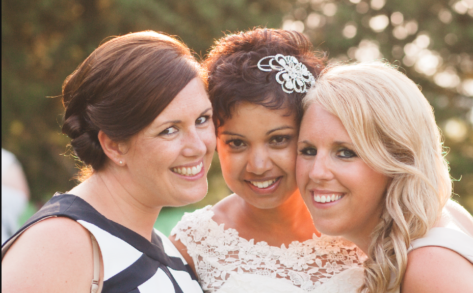 Three wedding guests share a joyful moment together outdoors.