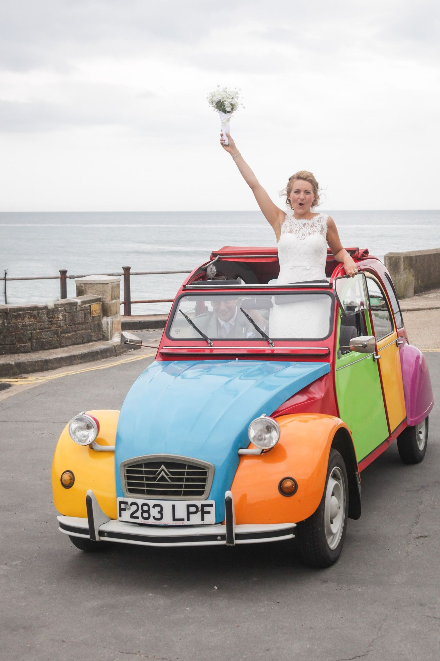 A rainbow-colored classic Citroen 2CV parked by the seaside.