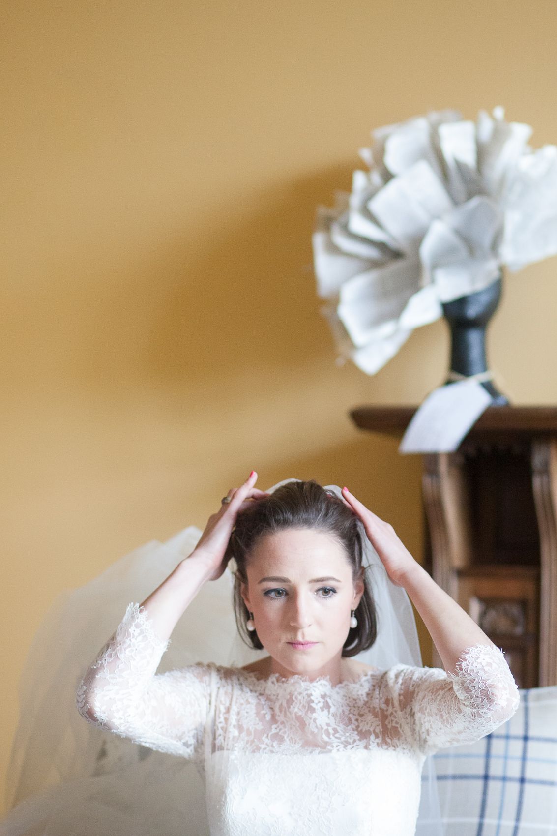 Bride adjusts white veil while getting ready against golden wall.