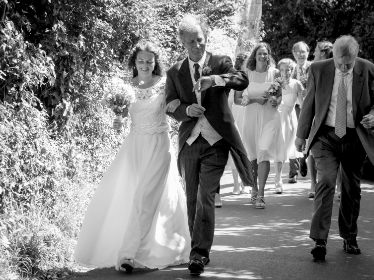 A black and white photo of wedding guests walking along a garden path.