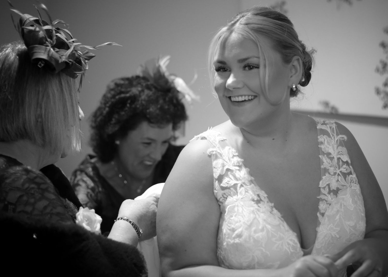 A bride in a lace wedding dress shares a candid black and white moment with wedding guests.